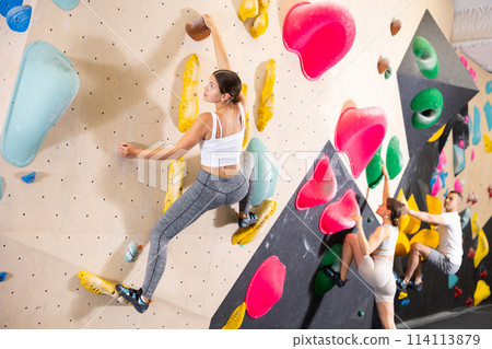 Motivated girl climbing without ropes on artificial bouldering wall 114113879