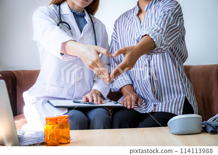 Doctor and patient woman hand do heart shape after explains the bottle of pills on the sofa at home and reports health examination results, medical checkup concept 114113988