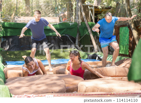 Cheerful people moving through obstacle course with soft pillows in pool of water Cheerful people moving through obstacle course with soft pillows in pool of water 114114110