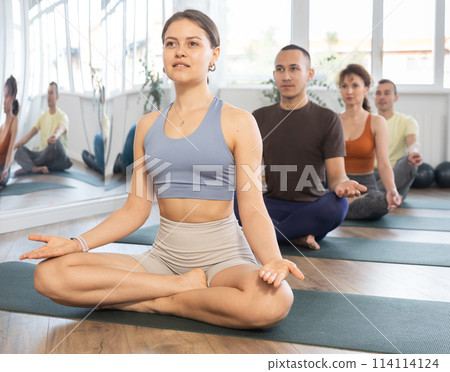 Girl yoga trainer perform doing traditional lotus position with group of students in gym 114114124