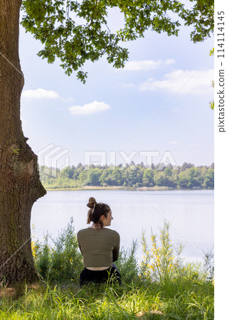 Pensive Woman Gazing at Lake from Shady Tree Spot 114114145