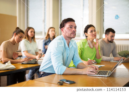 Handsome male student typing on laptop during lecture at university Handsome male student typing on laptop during lecture at university 114114153