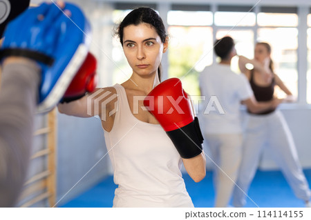 Young girl training boxing kicks on punch mitts held by instructor Young girl training boxing kicks on punch mitts held by instructor 114114155