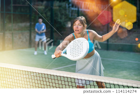 Young female paddle tennis player performing backhand on outdoor court 114114274