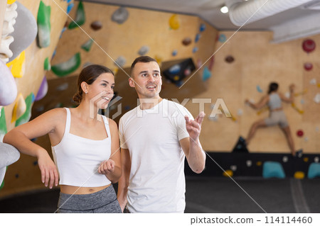 Girl gym coach and teen client standing in fitness room discussing possible options climbing Girl gym coach and teen client standing in fitness room discussing possible options climbing 114114460