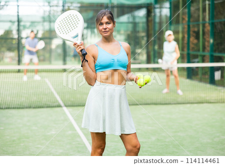 Positive girl looking at camera while playing padel at court Positive girl looking at camera while playing padel at court 114114461