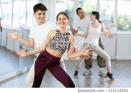 Group of young women and men enjoying active dance movement in studio 114114503