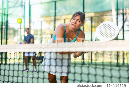 Young woman in skirt playing padel tennis on court 114114519