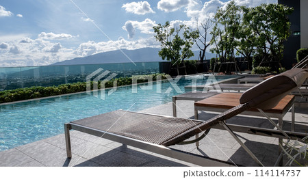 Picture of a sun bed chair on the edge of a hotel or resort rooftop swimming pool 114114737