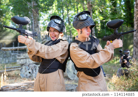 Young man and woman standing back-to-back on paintball field Young man and woman standing back-to-back on paintball field 114114885