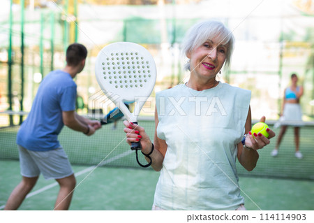 Portrait of positive senior woman on padel tennis court 114114903