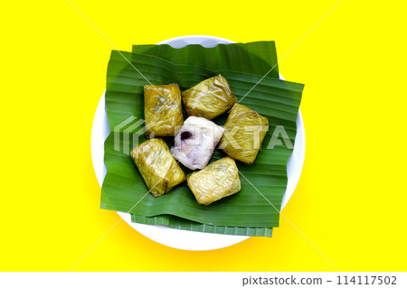 Bundled boiled sticky rice with banana and black beans wrapped in banana leaves 114117502