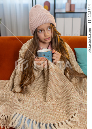 Sick ill girl child wrapped in blanket shivering from cold drinking hot herbal medical tea at home Sick ill girl child wrapped in blanket shivering from cold drinking hot herbal medical tea at home 114118744