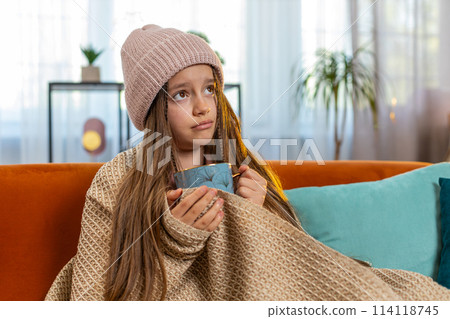 Sick ill girl child wrapped in blanket shivering from cold drinking hot herbal medical tea at home Sick ill girl child wrapped in blanket shivering from cold drinking hot herbal medical tea at home 114118745