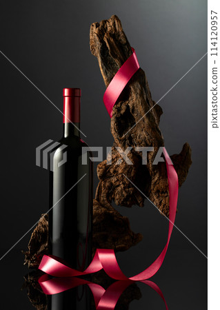 Bottle of red wine and old weathered snag with red satin ribbon. 114120957