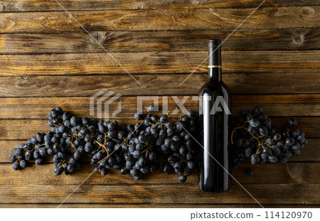 Blue grapes and bottle of red wine on an old wooden table. 114120970
