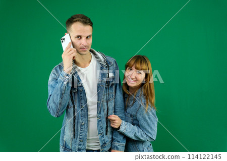 Cheerful guy and girl in denim clothes, couple, family. guy calling on the phone on a green background. High quality photo 114122145