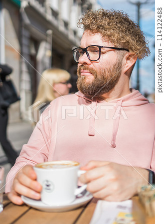 Millennial bearded man having breakfast at table of street cafe on spring day, drinking warm cappuccino. Spring restaurant terrace Millennial bearded man having breakfast at table of street cafe on spring day, drinking warm cappuccino. Spring restaurant terrace 114122488