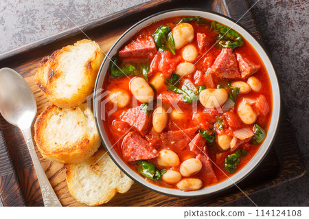 Spanish stew of butter beans, chorizo and spinach in tomato sauce close-up in a bowl. Horizontal top view 114124108
