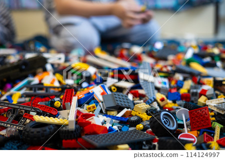 There are a large number of parts lying on the floor, and a child is sitting in the background. A child in a children's room plays with and collects different toys. 114124997