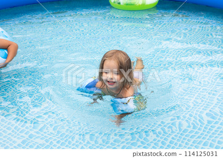 Children swim in an inflatable pool in the backyard of a house On a hot summer day children escape the heat in the cool water of an inflatable pool. Children have fun swimming in the inflatable pool. 114125031