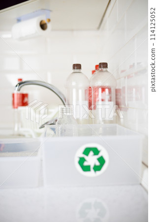 Plastic bottles stand in the kitchen against the backdrop of trash cans. Plastic bottles are washed and packed into boxes for recycling. The concept of environmental friendliness, plastic recycling. Plastic bottles stand in the kitchen against the backdrop of trash cans. Plastic bottles are washed and packed into boxes for recycling. The concept of environmental friendliness, plastic recycling. 114125052