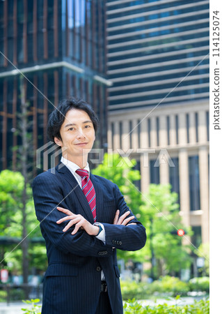 Businessman with arms folded in front of a skyscraper 114125074