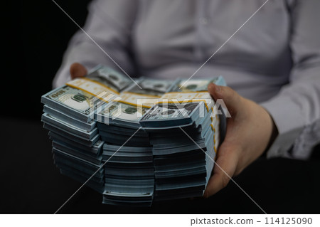 A businessman places stacks of dollars on the table in front of him. A man places stacks of hundred dollar bills on the table in front of him. Counting money on a black background. A businessman places stacks of dollars on the table in front of him. A man places stacks of hundred dollar bills on the table in front of him. Counting money on a black background. 114125090