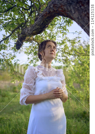 beautiful woman in white vintage dress with train in spring garden at sunset 114125138