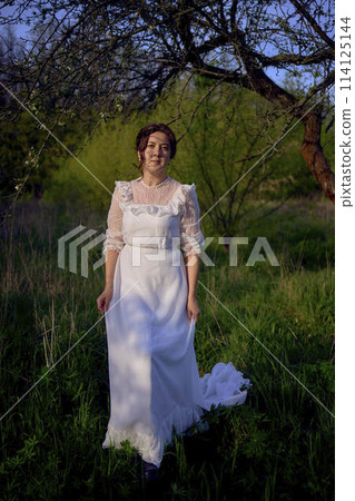 beautiful woman in white vintage dress with train in spring garden at sunset beautiful woman in white vintage dress with train in spring garden at sunset 114125144