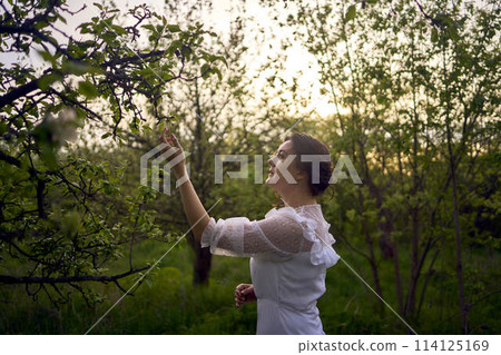 beautiful woman in white vintage dress with train in spring garden at sunset beautiful woman in white vintage dress with train in spring garden at sunset 114125169