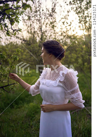 beautiful woman in white vintage dress with train in spring garden at sunset beautiful woman in white vintage dress with train in spring garden at sunset 114125171