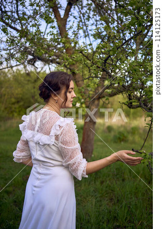beautiful woman in white vintage dress with train in spring garden at sunset beautiful woman in white vintage dress with train in spring garden at sunset 114125173