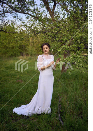 beautiful woman in white vintage dress with train in spring garden at sunset 114125176