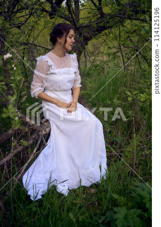beautiful woman in white vintage dress with train in spring garden at sunset 114125196