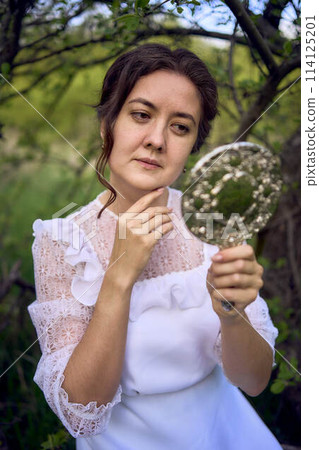 beautiful woman in white vintage dress with train and holding vintage mirror in spring garden at sunset beautiful woman in white vintage dress with train and holding vintage mirror in spring garden at sunset 114125201