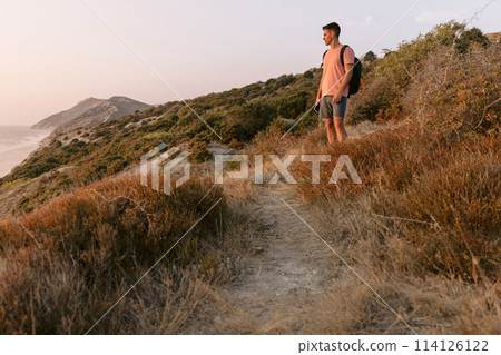Traveler man with backpack walking on sea coastline with warm sun light. Traveler man with backpack walking on sea coastline with warm sun light. 114126122