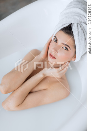 Attractive girl with open eyes takes a milk bath, touching her face 114126168