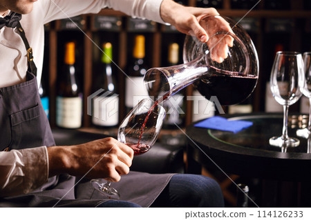 Skilled sommelier pouring wine from decanter ino wine glass. 114126233