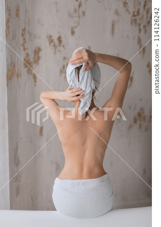 Young woman with naked back wearing towel on head, sitting on bathtub edge. Young woman with naked back wearing towel on head, sitting on bathtub edge. 114126242