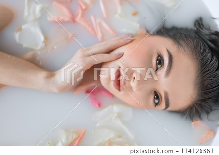 Close-up of female face relaxing in milky white water, looking at camera Close-up of female face relaxing in milky white water, looking at camera 114126361