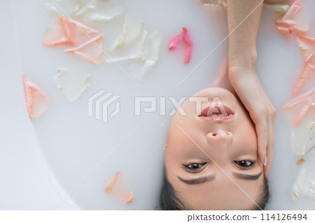 Close-up of female face relaxing in milky white water, looking at camera Close-up of female face relaxing in milky white water, looking at camera 114126494