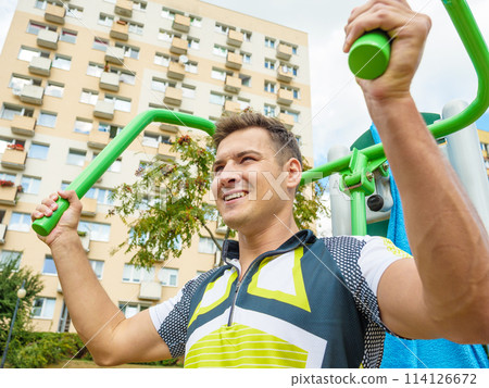 Man flexing arm on outdoor gym machine 114126672
