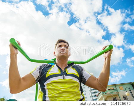 Man flexing arm on outdoor gym machine 114126673