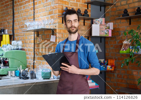 Young man in apron, food service worker, small business owner entrepreneur with work papers 114126826