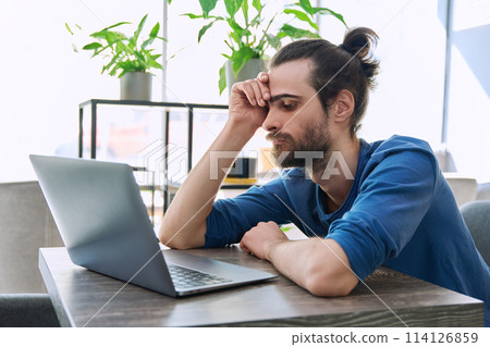 Serious tired young man looking at laptop screen 114126859