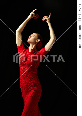 Elegant woman in beautiful red dress performing with castanets against black background. Following Spanish traditions 114126973