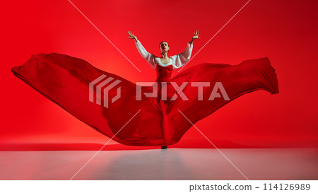 Passionate woman, flamenco dancer in stylish costume with skirt spreads like wings, performing against vivid red background 114126989