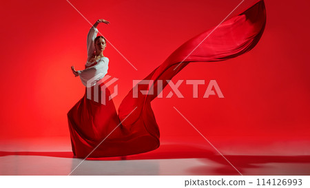 Passionate and elegant woman in vivid stage costume making creative performance against bright red background Passionate and elegant woman in vivid stage costume making creative performance against bright red background 114126993