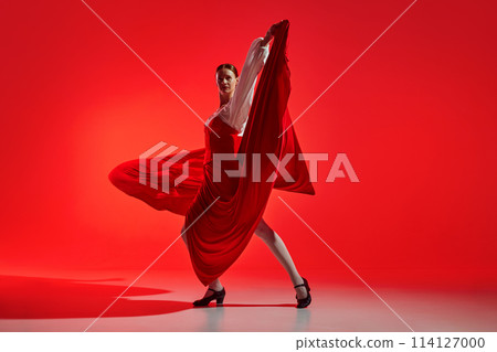Female artistic flamenco dancer showing passion against striking red background. Elegant pose and flowing skirt showing intense emotions of dance. 114127000